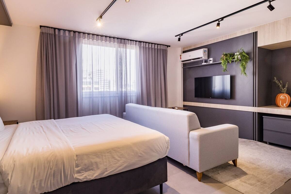 Quarto moderno com cama, sofá, televisão e área de trabalho.