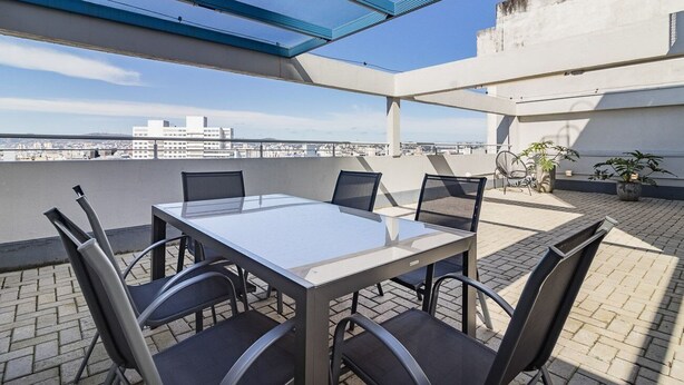 A rooftop terrace with a glass table and chairs, a blue canopy, and a view of the cityscape. - Duque by My Way (Porto Alegre)