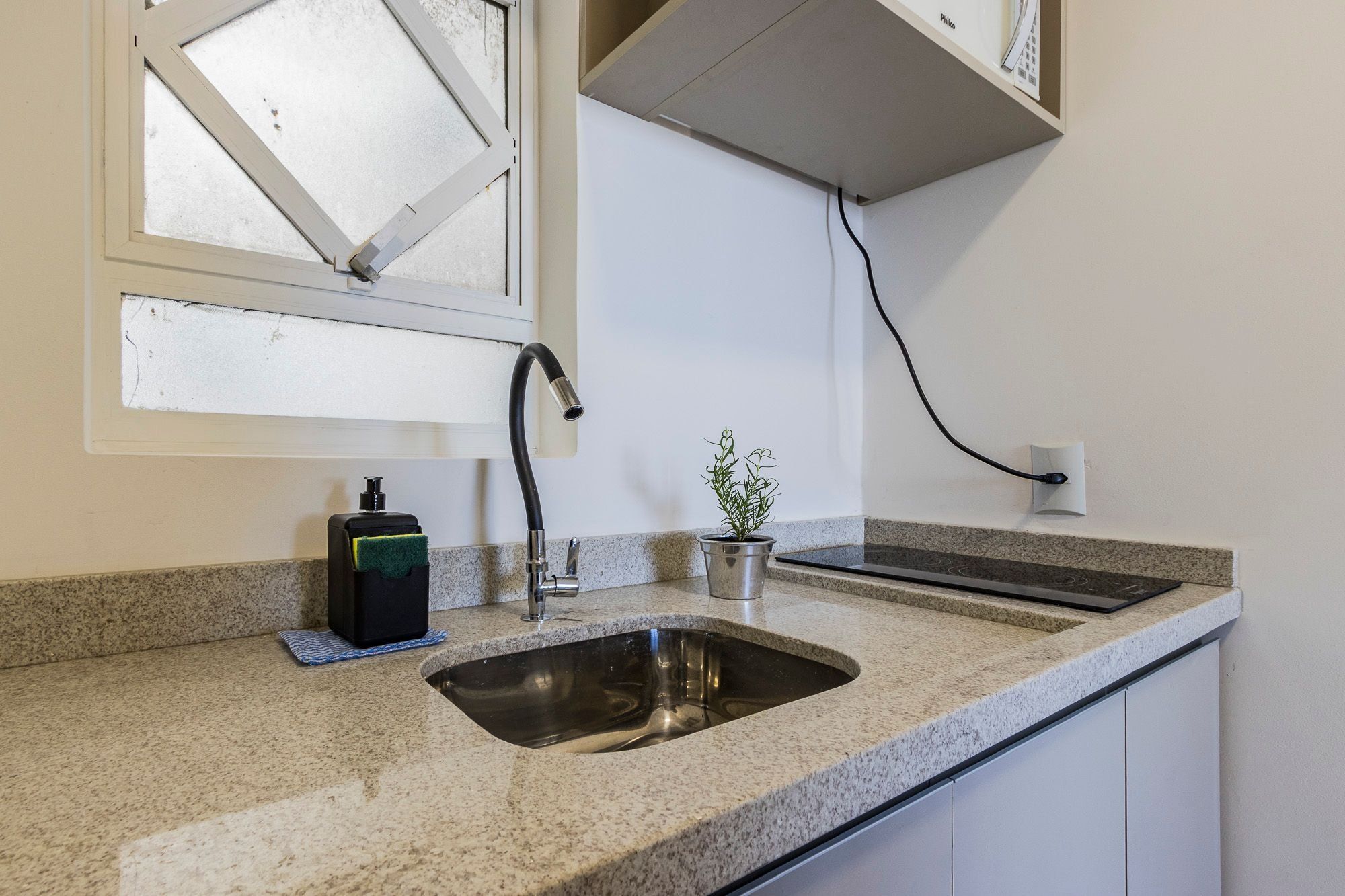 A kitchen with a granite countertop, a stainless steel sink, a faucet, a soap dispenser, and a potted plant.