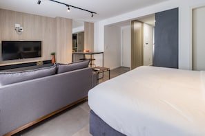 A modern hotel room with a large bed, a sofa, a TV, and a small table. - Duque by My Way (Porto Alegre)