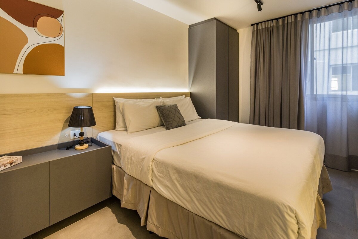 A hotel room with a bed, bedside table, lamp, and curtains.