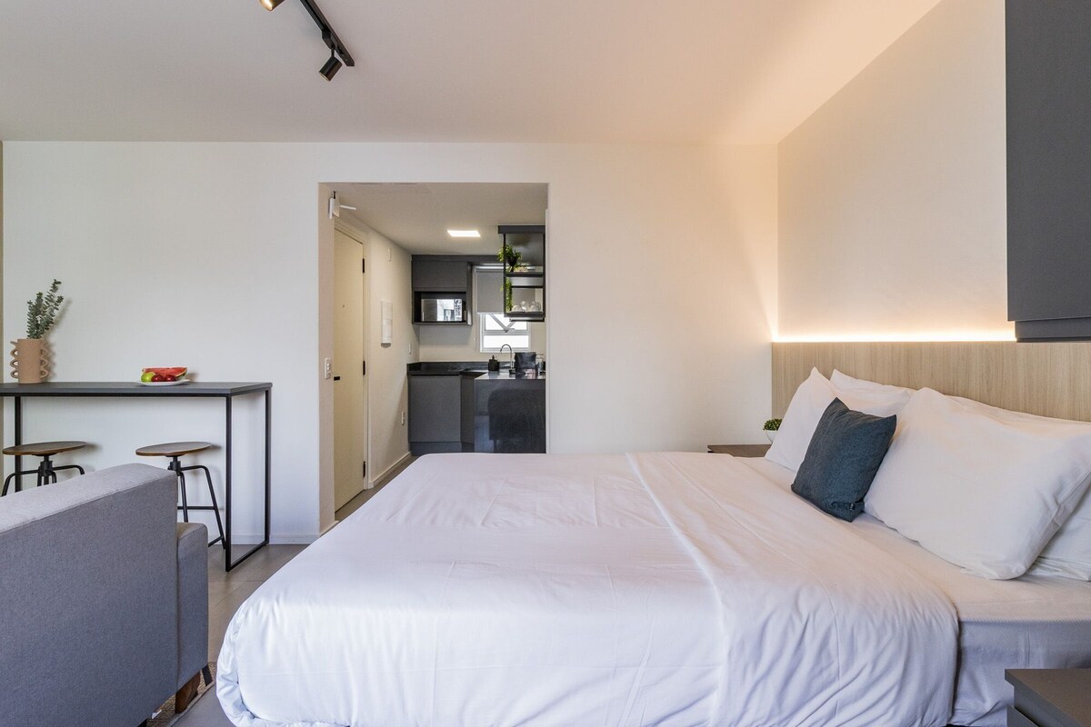 A hotel room with a bed, a desk, and a kitchenette.
