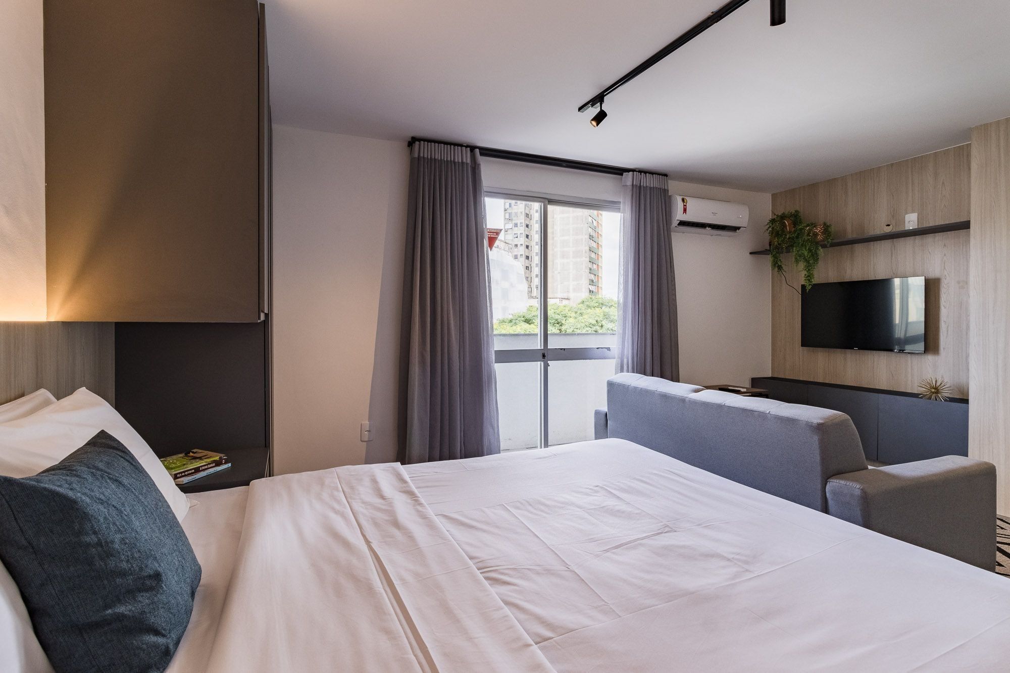 A modern hotel room with a large bed, a TV mounted on the wall, and a balcony with curtains.