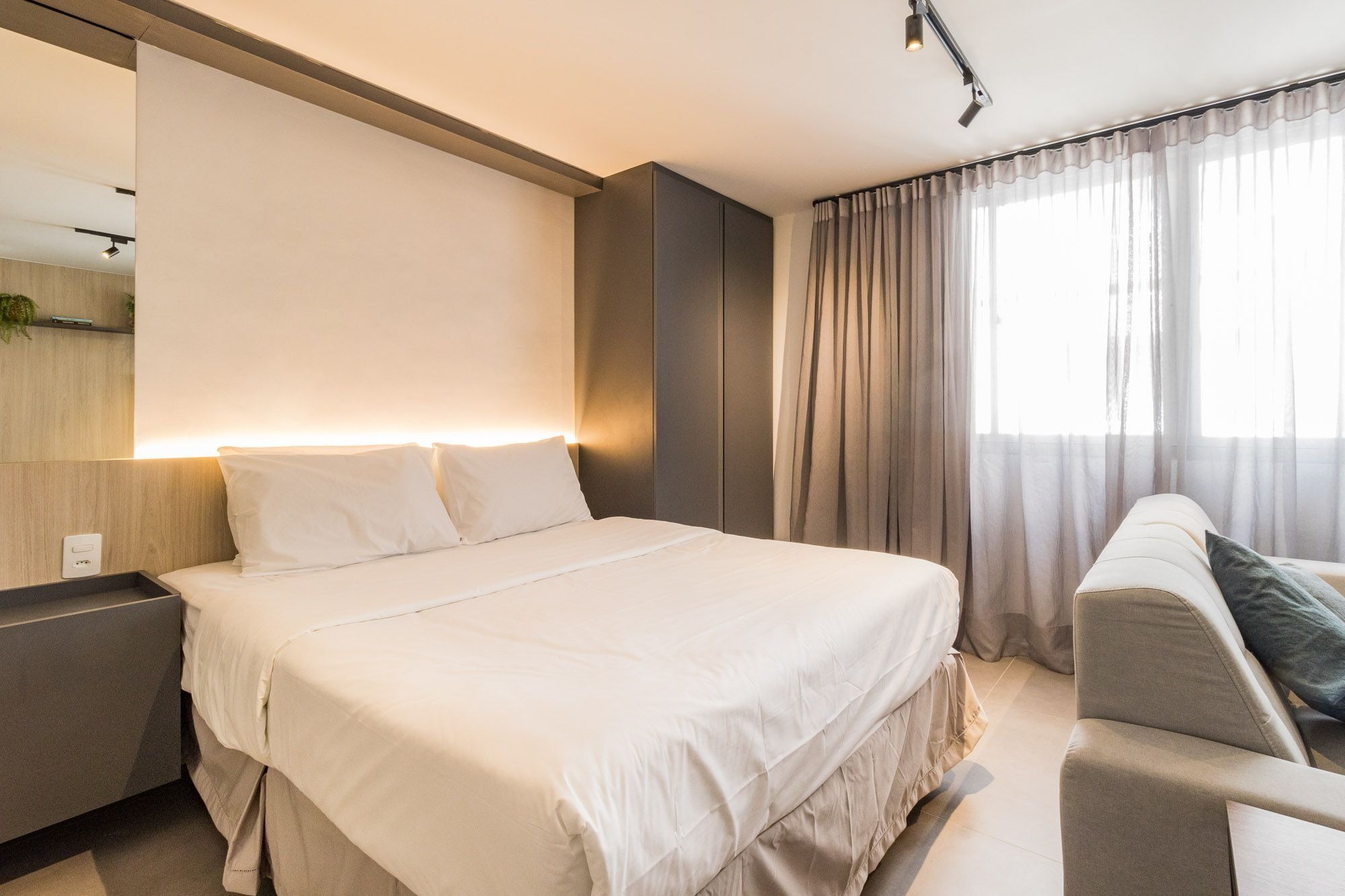 A modern hotel room with a large bed, a bedside table, a chair, and a large window with curtains.