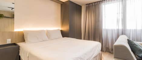A modern hotel room with a large bed, a bedside table, a chair, and a large window with curtains.