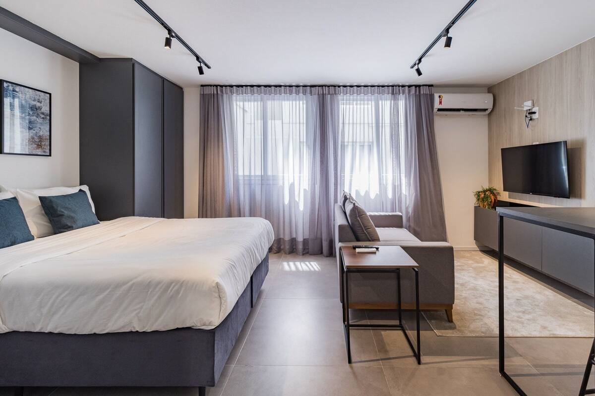 Quarto de hotel moderno com cama, sofá, televisão e ar condicionado.