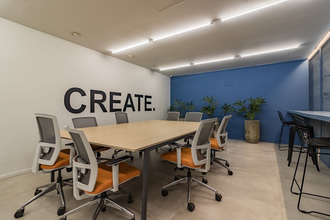 A conference room with a large table, six chairs, and a blue accent wall with the word 'CREATE.'