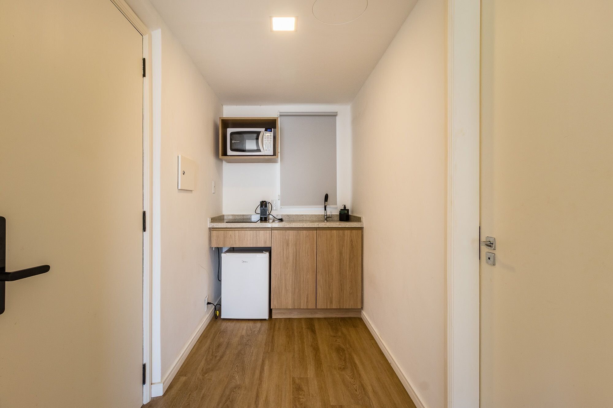 A narrow hallway leading to a compact kitchenette with a microwave, sink, and small refrigerator.