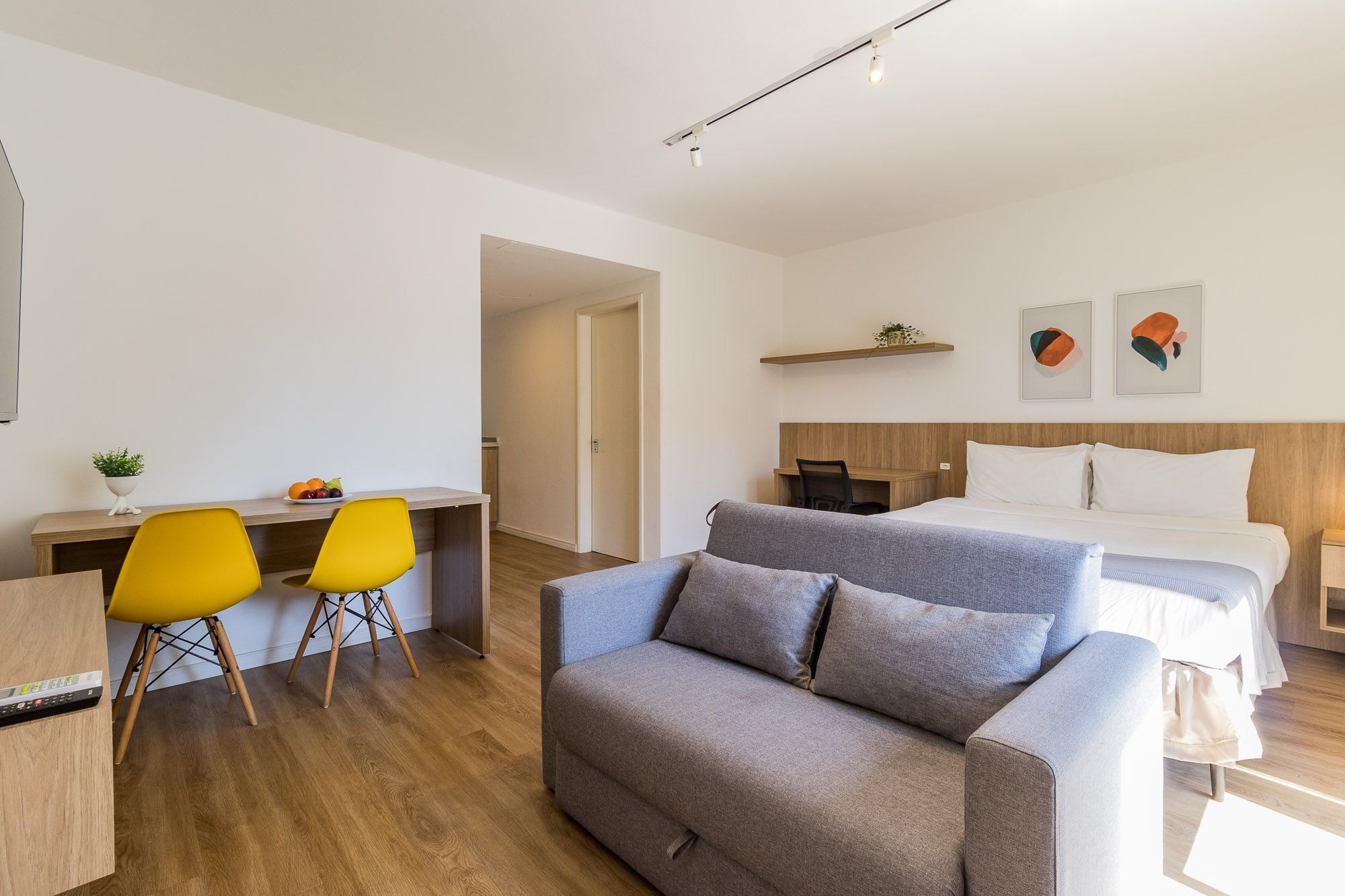 A modern hotel room with a bed, a sofa, a desk with two chairs, and a small plant.