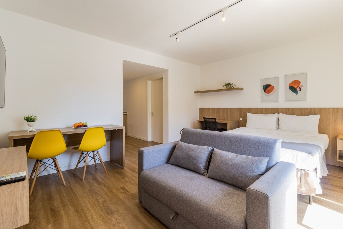 Une chambre d’hôtel moderne comprenant un lit, un canapé, un bureau avec deux chaises et une petite plante.