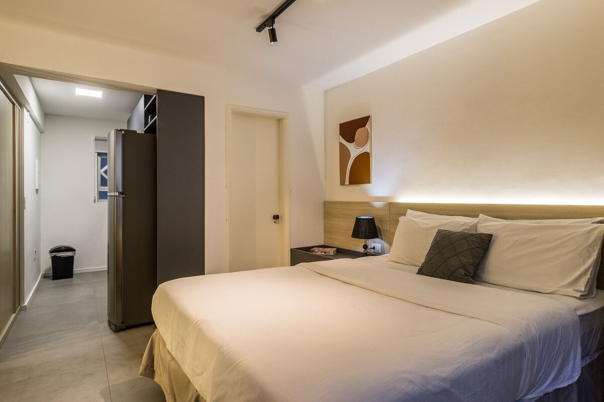 A hotel room with a bed, bedside table, lamp, and a wall art piece.