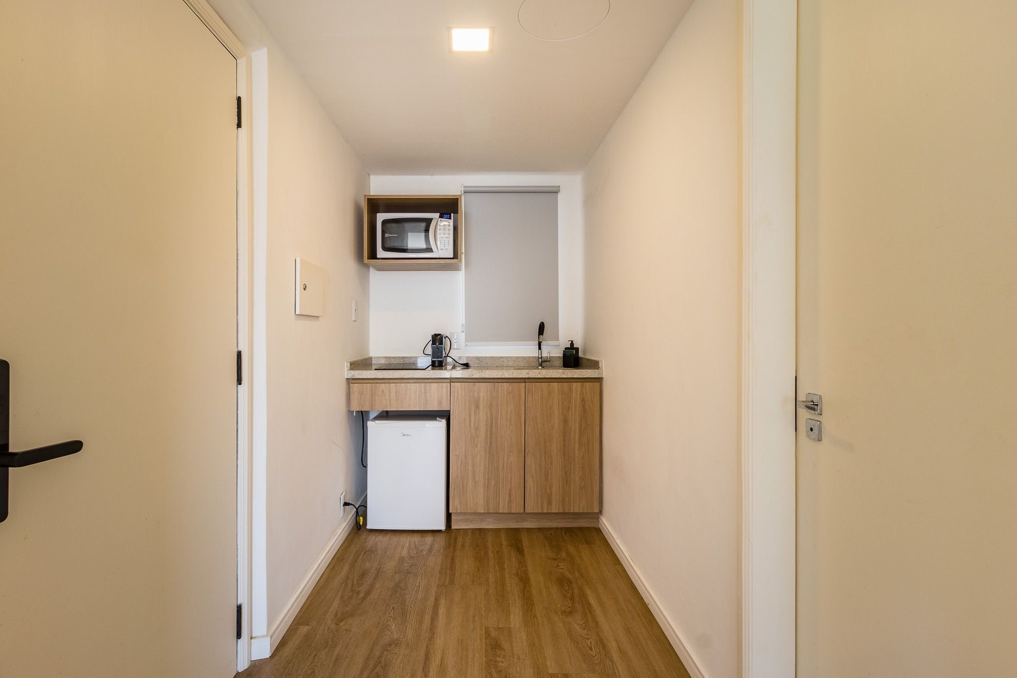 A narrow hallway leading to a compact kitchenette with a microwave, sink, and small refrigerator.