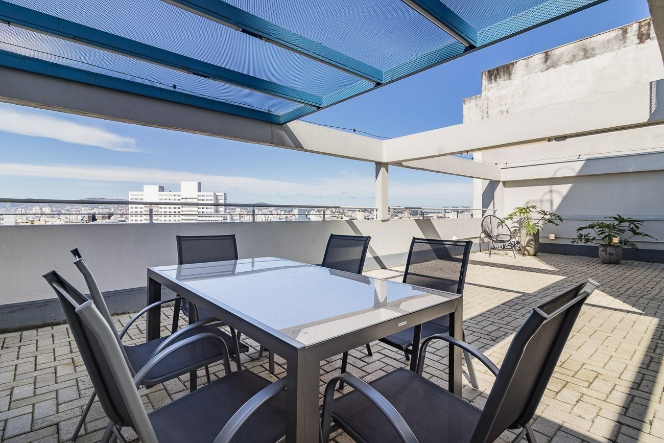 A rooftop terrace with a glass table and chairs, a blue canopy, and a view of the cityscape.