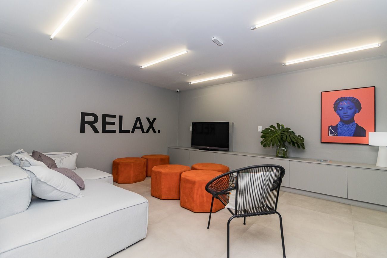 A modern living room with a white sofa, orange ottomans, a black chair, a flat-screen TV, and a wall-mounted plant.