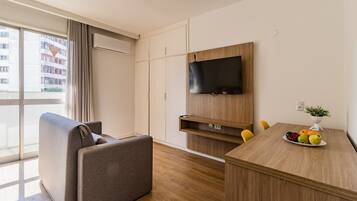 A modern hotel room with a sofa, a dining table with fruit, a TV, and a wardrobe.