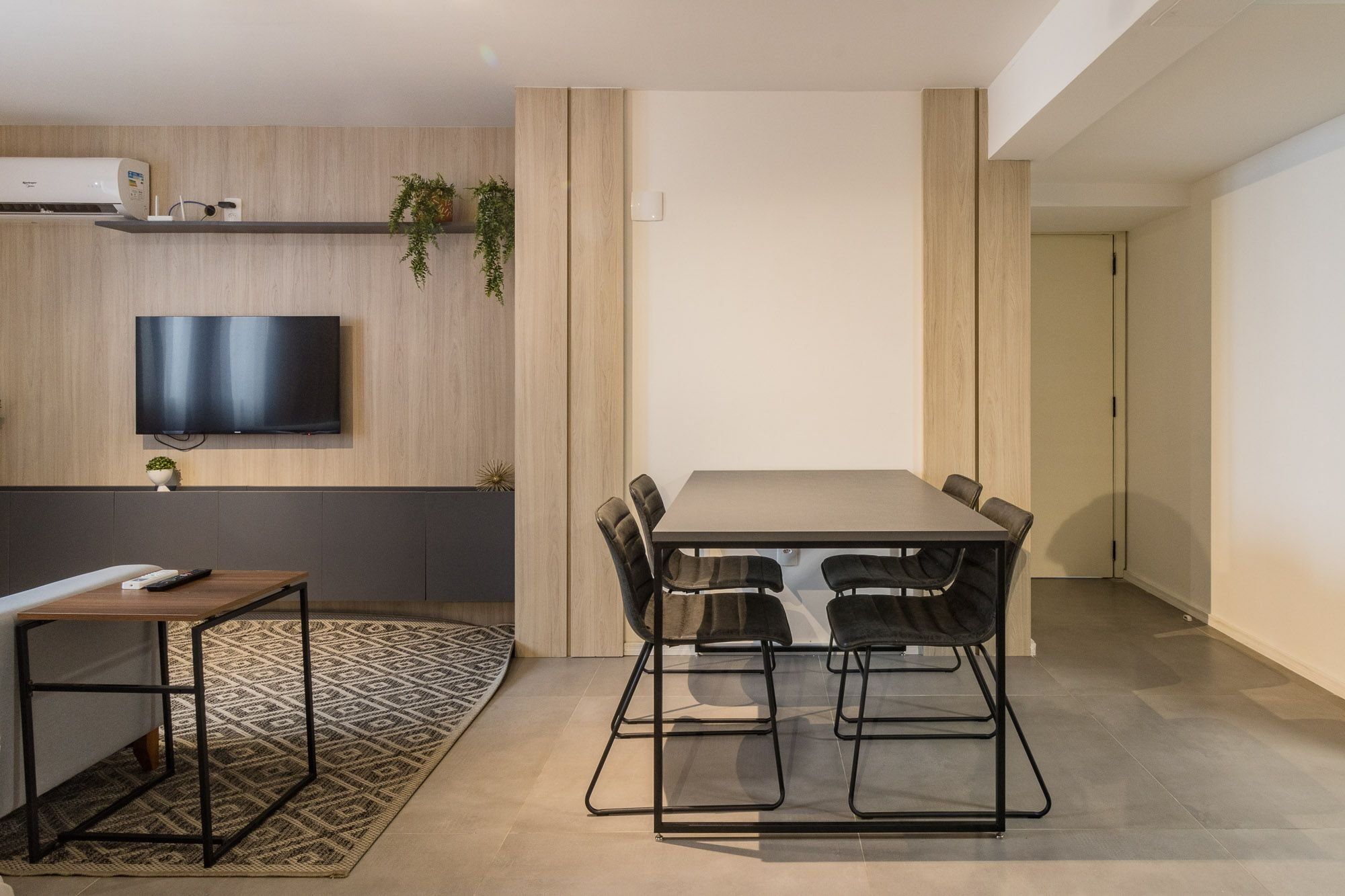 Uma sala de estar moderna com televisão de tela plana, uma mesa de jantar com cadeiras, uma pequena mesa lateral e um tapete estampado.