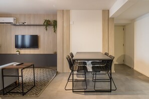 Un salon moderne avec un téléviseur à écran plat, une table à manger avec des chaises, une petite table d’appoint et un tapis à motifs.