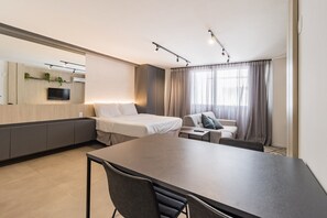 A modern hotel room with a bed, a sofa, a dining table, and a TV. - Duque by My Way (Porto Alegre)