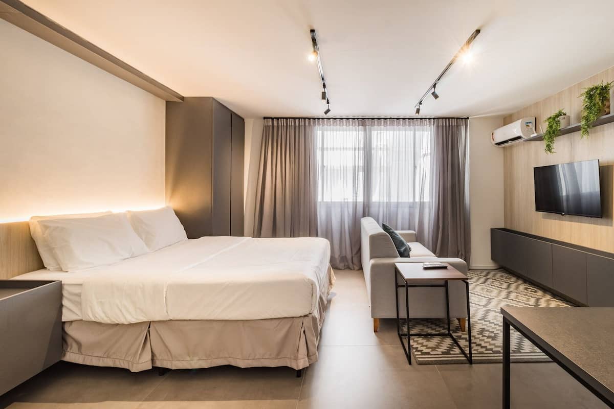 Quarto de hotel moderno com cama, sofá, televisão e escrivaninha.