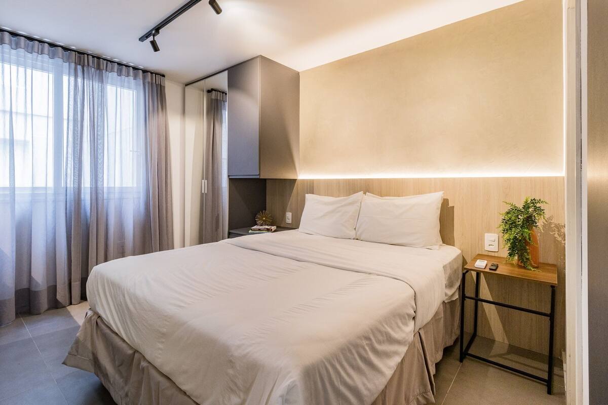 Quarto de hotel moderno com uma cama grande, mesa de cabeceira e um espelho.