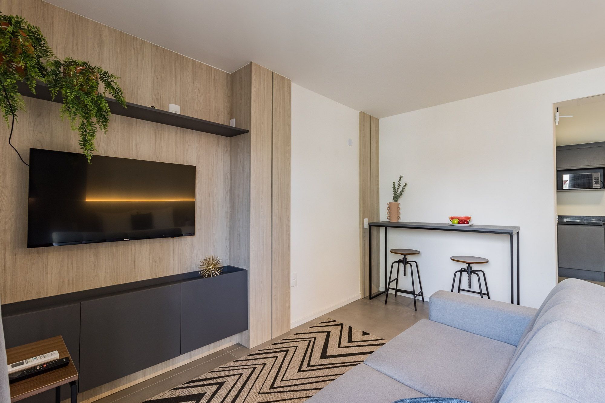 Uma sala de estar moderna com televisão de tela plana, um sofá, uma mesa de centro e uma área de cozinha com micro-ondas.