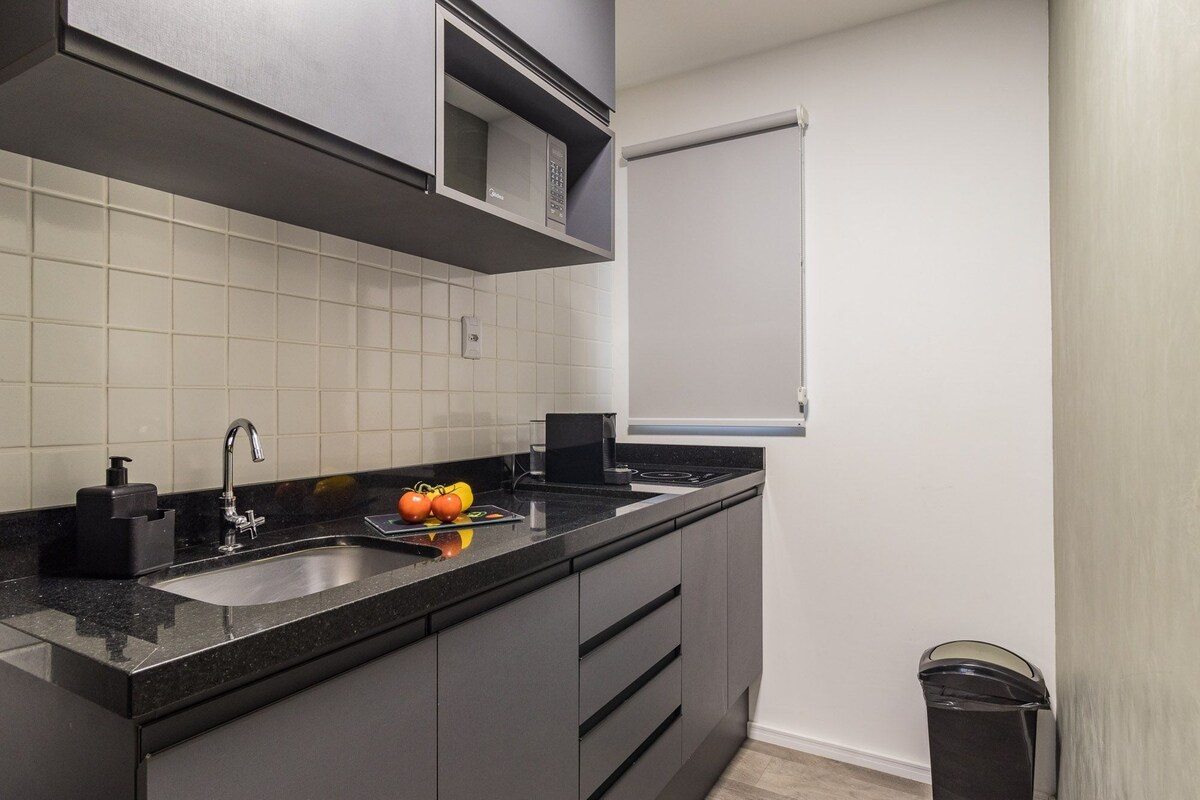 Une cuisine moderne avec un plan de travail noir, un évier en acier inoxydable et un four à micro-ondes placé au-dessus de la cuisinière.
