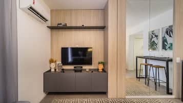Uma sala de estar moderna com televisão de tela plana, um rack cinza, uma mesinha lateral e um espaço de jantar com um banco de balcão.