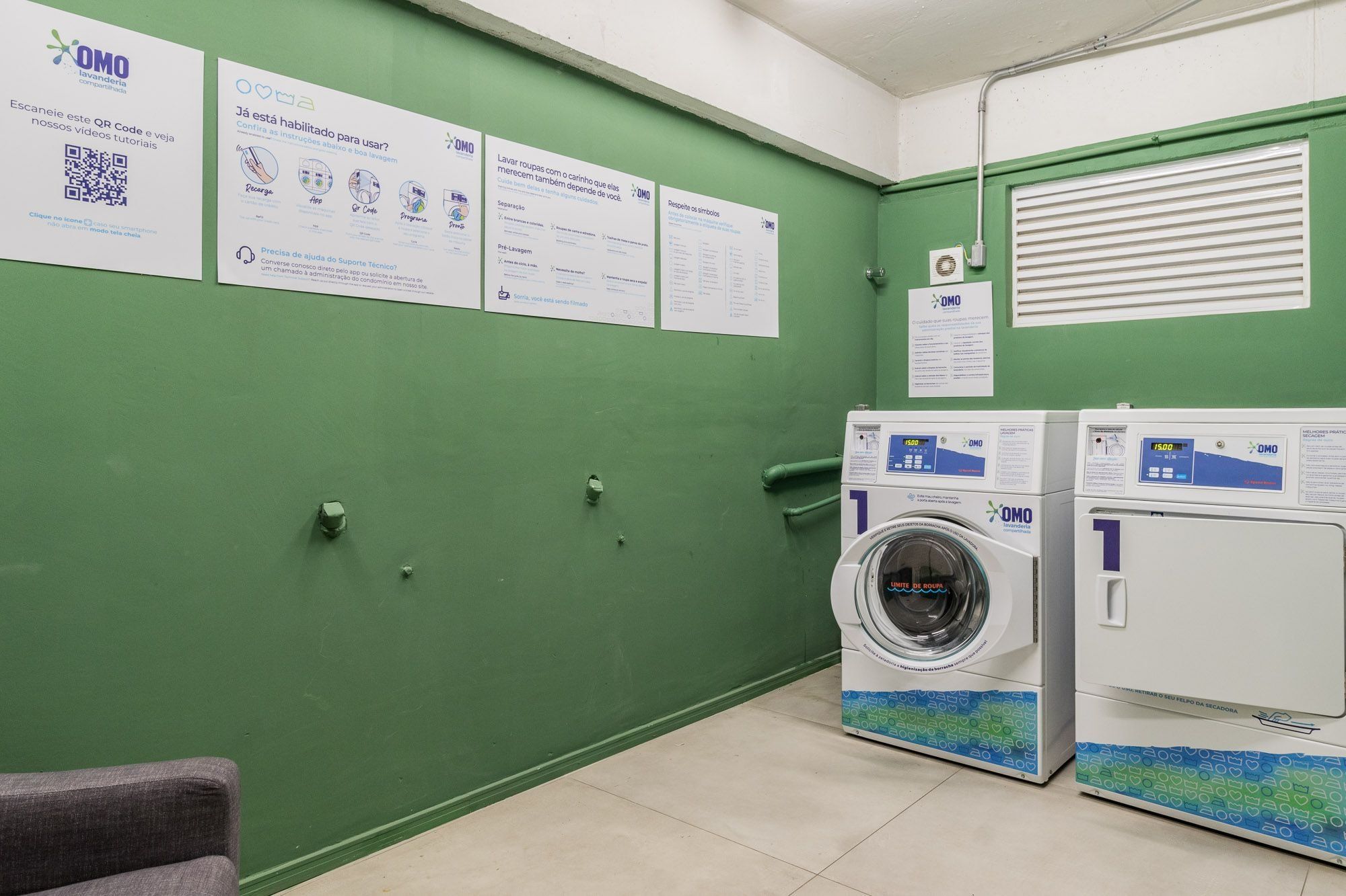 Una sala de lavandería con paredes verdes, dos lavadoras y carteles informativos.