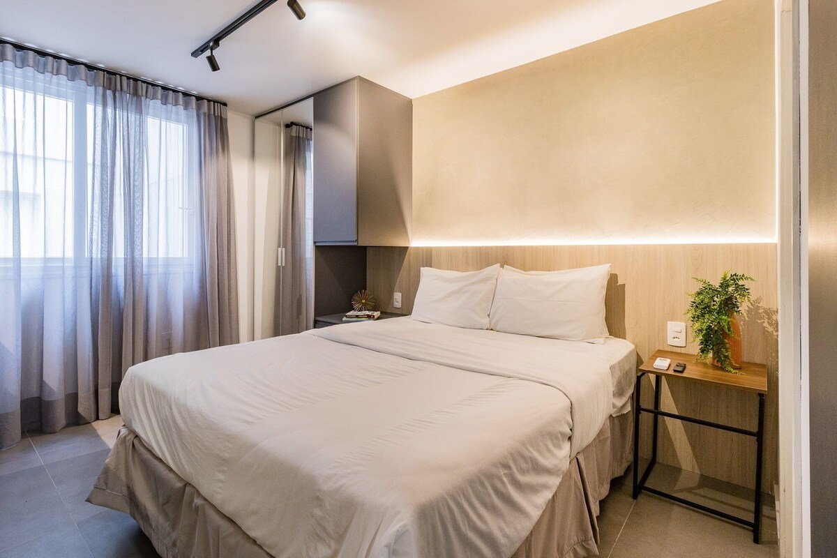 A modern hotel room with a large bed, bedside table, and a mirror.