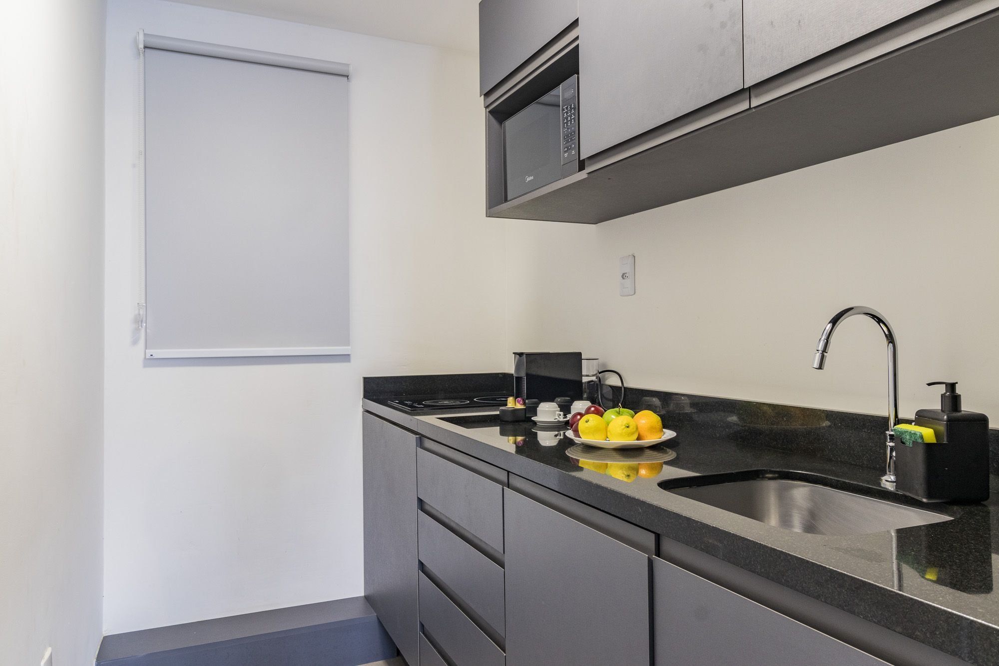 A compact kitchen with a built-in microwave, a sink, and a countertop with a fruit bowl.