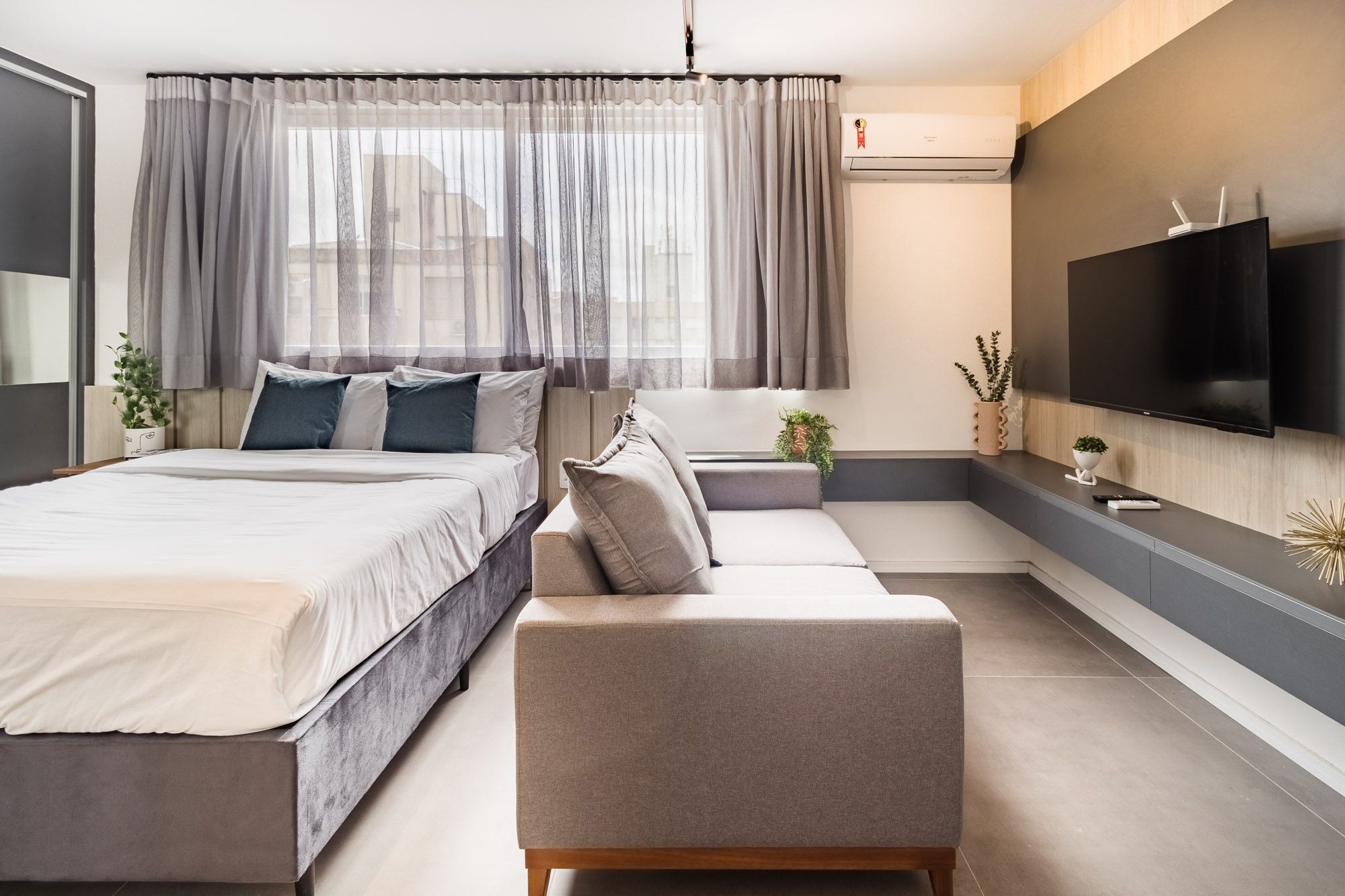 Quarto moderno com cama, sofá, televisão e aparelho de ar condicionado.