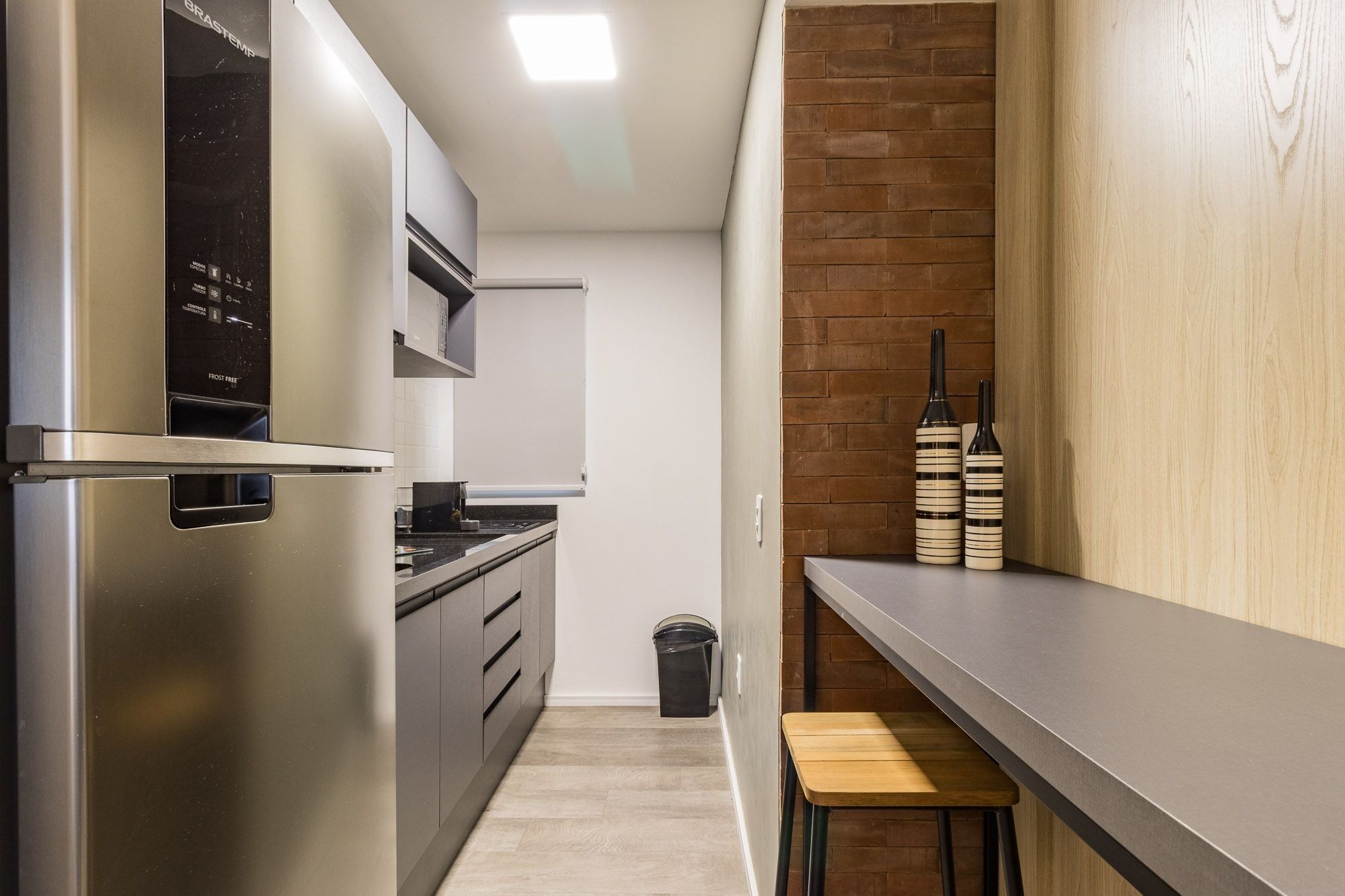 A modern kitchen with a stainless steel refrigerator, a microwave, and a stove. There is a wooden bench and two decorative bottles on the counter.