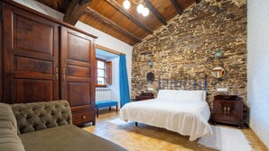A bedroom with a bed, wooden wardrobe, bench, and stone wall. - A Painza Aldea Rural  (Arzua)