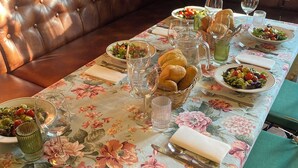 A dining table set with floral tablecloth, plates of food, glasses, and bread baskets. - A Painza Aldea Rural  (Arzua)