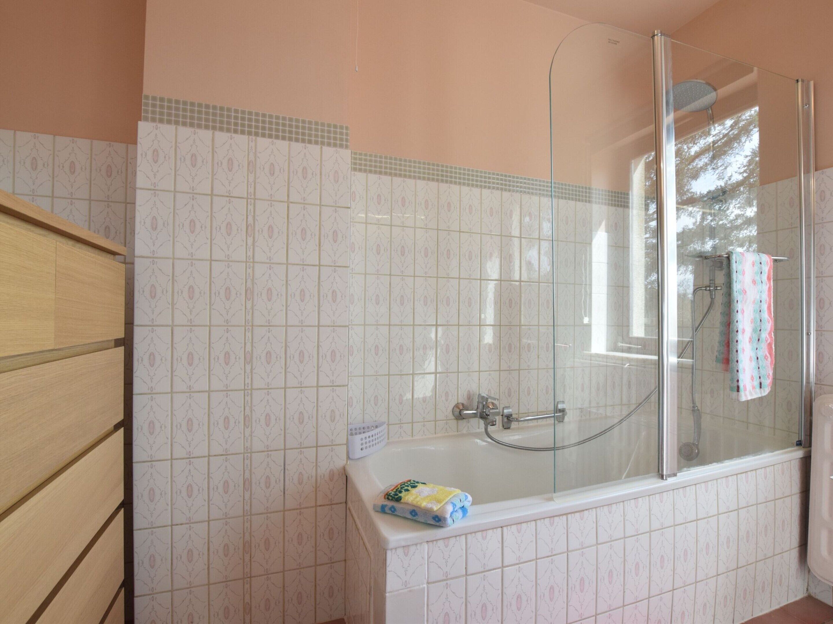 Een badkamer met een douchekabinet van glas, een bad met een handdoek, en betegelde vloeren.