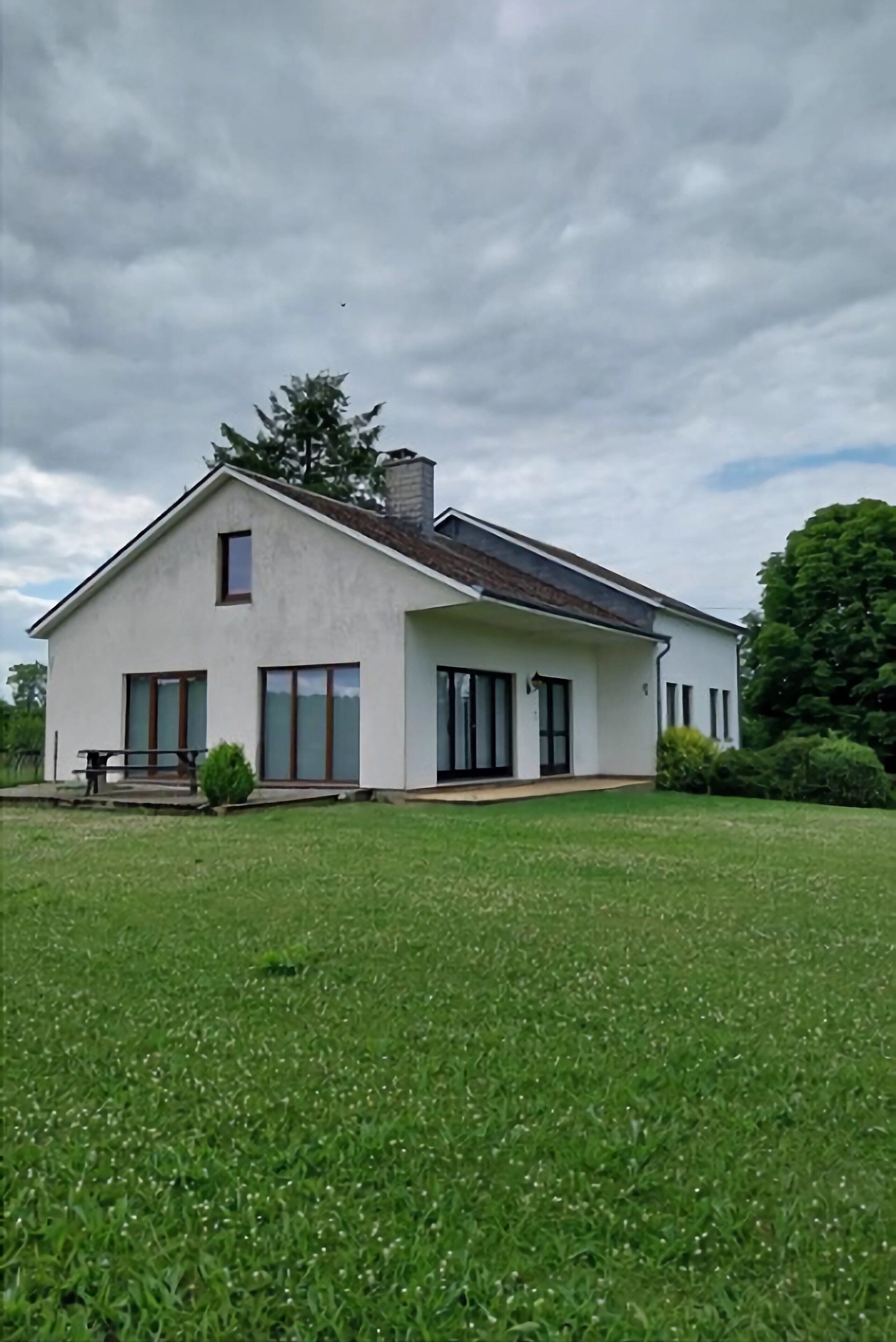 Une maison moderne avec une grande pelouse, une cheminée et un petit porche.