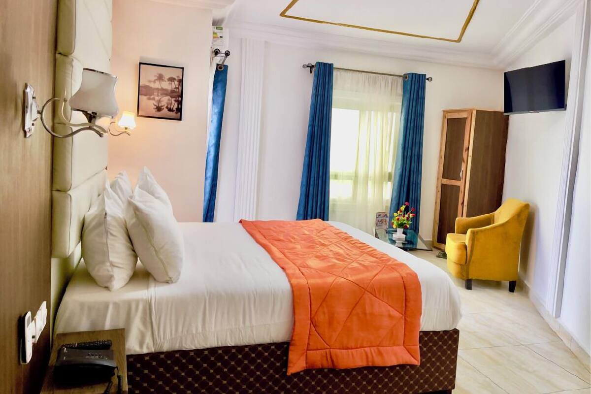 Quarto de hotel com uma cama, televisão, poltrona amarela e guarda-roupa.