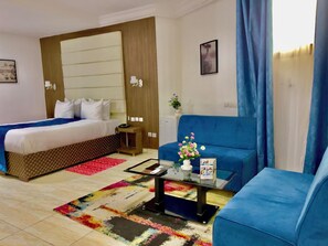 A hotel room with a bed, a blue sofa, a coffee table, and a colorful rug. - Hotel Vent et Maree (Douala)