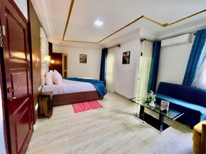 A hotel room with a bed, a glass coffee table, a sofa, and a door. - Hotel Vent et Maree (Douala)