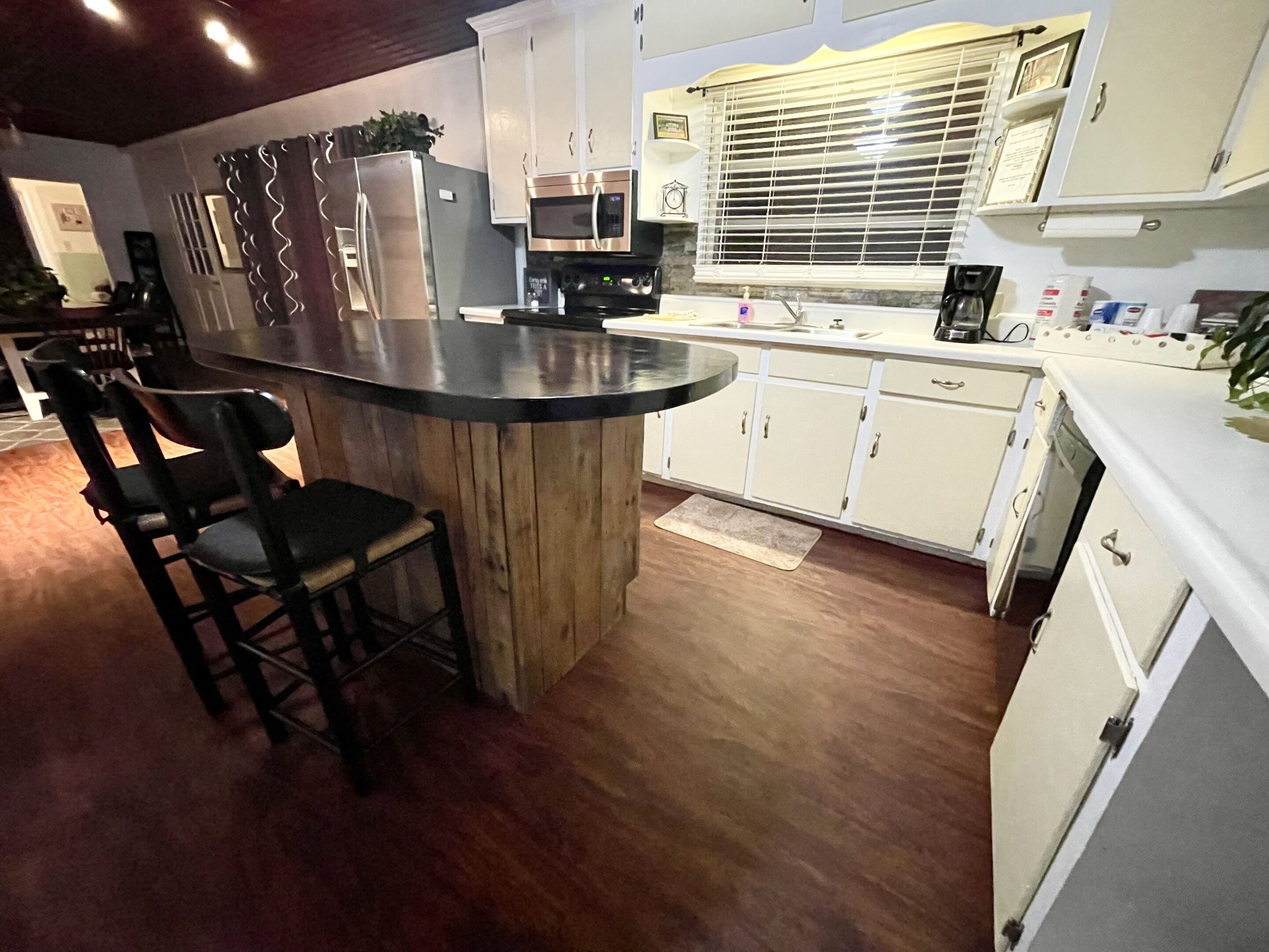 A kitchen with a central island, bar stools, white cabinets, and a window with blinds.