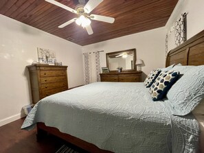 A bedroom with a bed, a dresser, a ceiling fan, and a mirror.