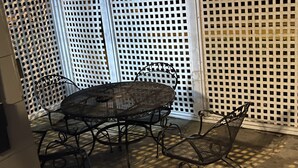 An outdoor patio with a round metal table and four chairs, surrounded by a white lattice fence.