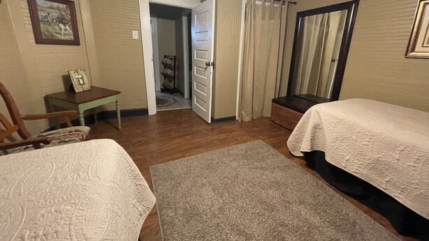 A bedroom with two beds, a desk, a chair, and a door leading to another room.