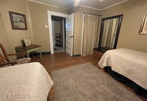 Een slaapkamer met twee bedden, een bureau, een stoel en een deur naar een andere kamer.