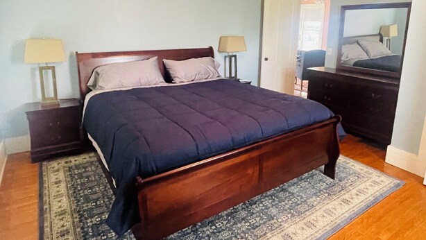 A bedroom with a wooden bed, two bedside tables with lamps, a dark-colored headboard, and a patterned rug on the floor. - Cozy 1-bedroom apartment with WiFi, AC, full kitchen, in enjoyable Colebrook (Colebrook)