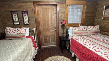 Una habitación con dos camas, una puerta de madera, una ventana con persianas y una mesita de noche con lámpara.