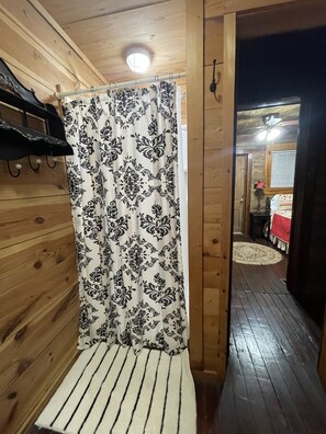 A wooden interior with a shower curtain, a bench, and a hallway leading to another room. - Row Cottages Honeysuckle Cottage (Hartsfield)