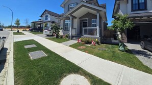 A residential street with houses, a sidewalk, and a grassy area.