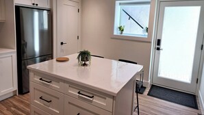 A modern kitchen with white cabinetry, a stainless steel refrigerator, a marble countertop, and a small potted plant.