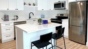 A modern kitchen with white cabinets, stainless steel appliances, a central island with bar stools, and a microwave above the oven.